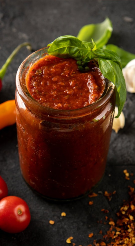 Jar of our homemade traditional sauce with a sprig of basil on the rim.